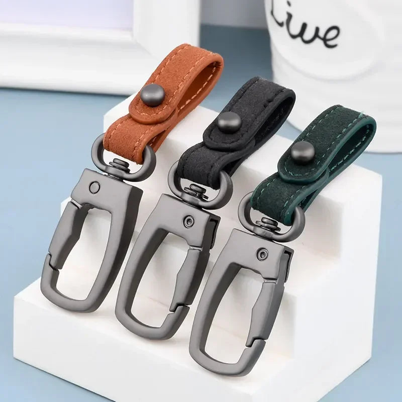 A set of genuine leather keyring keychains in brown, black, and dark green colors displayed on a white block.