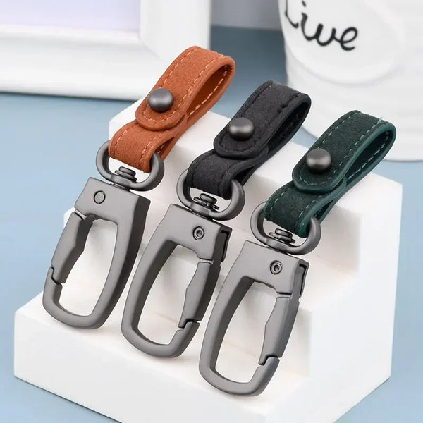A set of genuine leather keyring keychains in brown, black, and dark green colors displayed on a white block.
