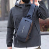 A person wearing a dark gray jacket is carrying a black anti-theft crossbody chest bag on their shoulder.