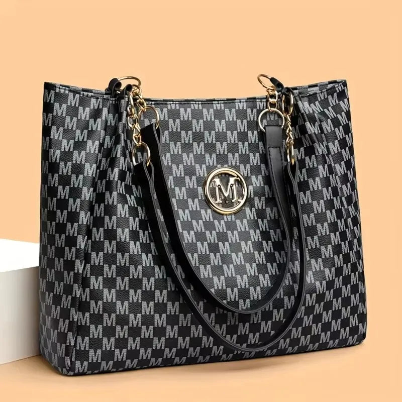 A black and white geometric monogram print tote bag with gold hardware shown against a light background.