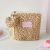 A fluffy leopard print makeup bag with a gold clasp and yellow cord, resting on a white surface.