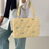 Bolso para portátil acolchado amarillo claro con detalles de lazo azul, llevado por una persona con camisa blanca y jeans.