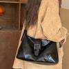A brown jacket holds a black PU leather underarm bag with a silver buckle.