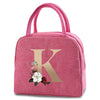 A pink insulated canvas lunch bag featuring a large gold letter K and a small floral design.