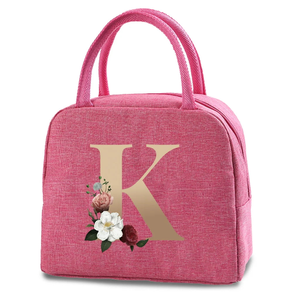 A pink insulated canvas lunch bag featuring a large gold letter K and a small floral design.