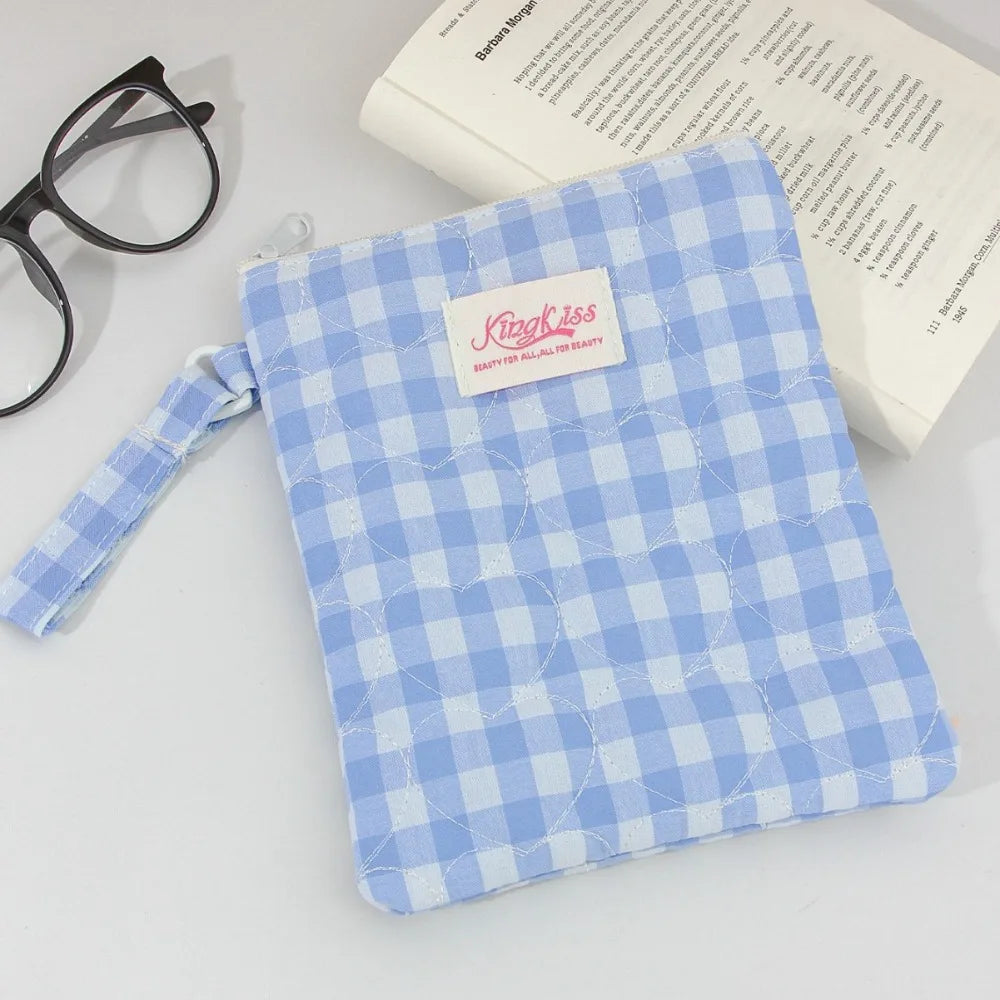 A light blue plaid cotton tablet pouch with a pink tag and a blue fabric tie is shown next to reading glasses and a book.