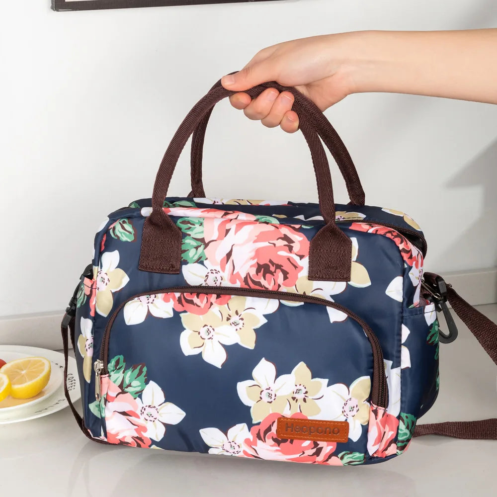 Una bolsa térmica portátil azul marino con estampado floral es sostenida por una mano.