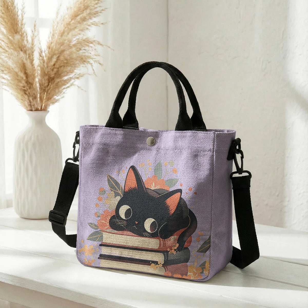 Lila Tasche mit Blumen-Katzenmuster (schwarze Katze und gestapelte Bücher) auf weißem Untergrund.