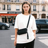 A young woman wearing a white t-shirt and black pants holds a black zippered phone pouch with a strap.