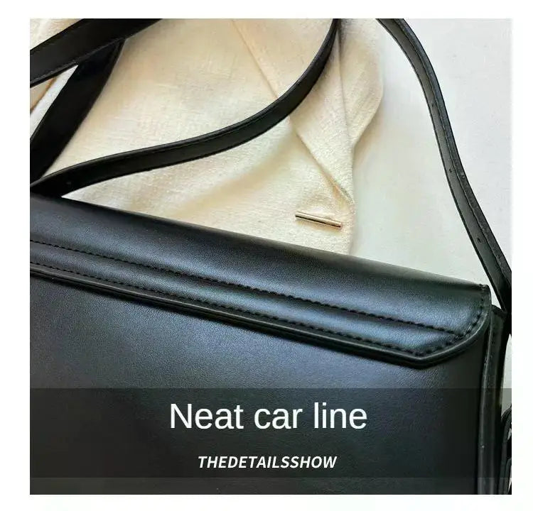 Bolso cruz de cuero negro con detalle de línea de coche contra fondo claro.