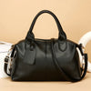 A black soft leather tote bag with a zipper closure and adjustable shoulder strap is shown against a beige background.