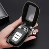 A hand holds an open black PU leather car key case with a metal hook and a clear plastic card inside.