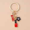 A gold-toned enamel heart keychain featuring a small heart charm and a black and gold flower charm.