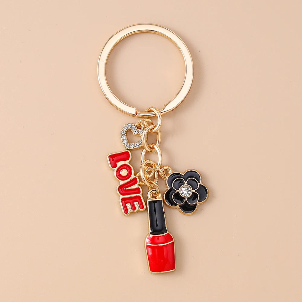 A gold-toned enamel heart keychain featuring a small heart charm and a black and gold flower charm.