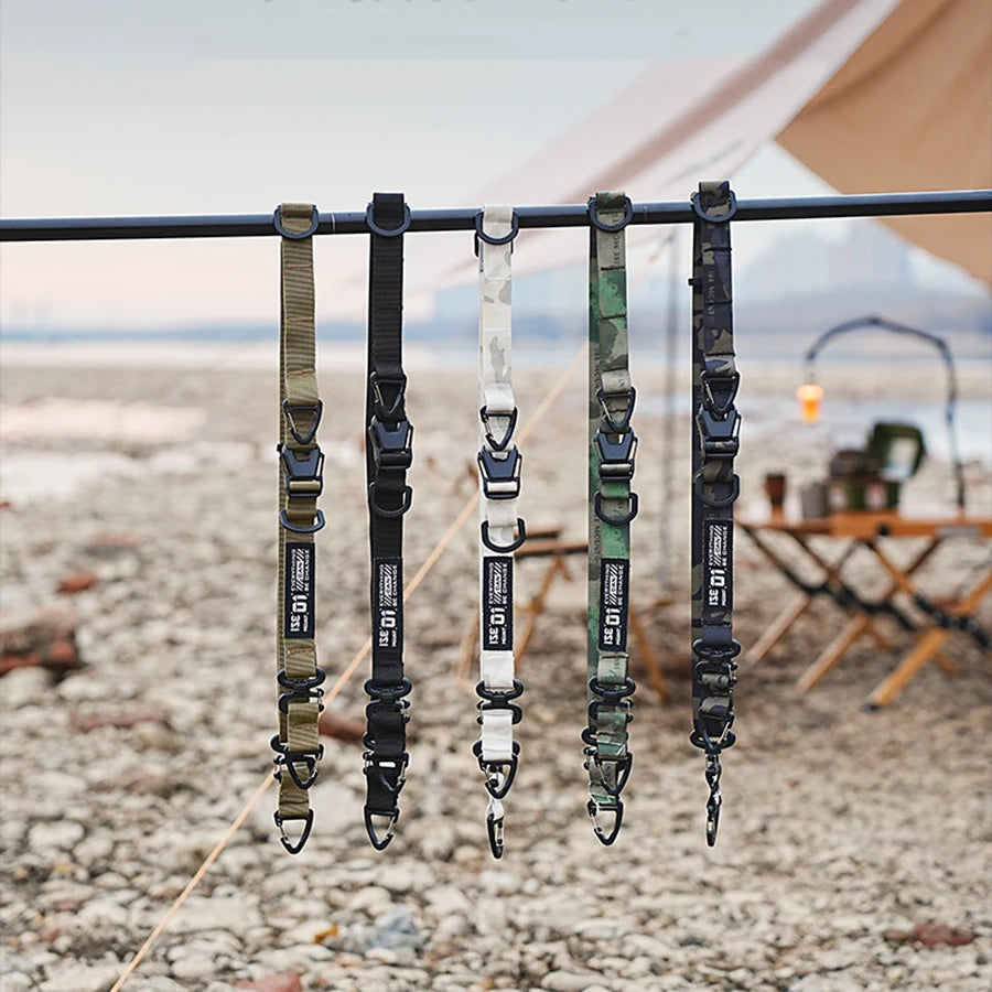 A close-up of a durable outdoor camping crossbody strap hanging on a clothesline against a neutral, arid background.