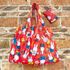 A bright orange and red Miffy folding shopping bag with a small matching pillow is displayed against a brick wall.