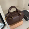 A brown vintage PU leather shoulder bag with gold hardware resting on a light wooden surface.