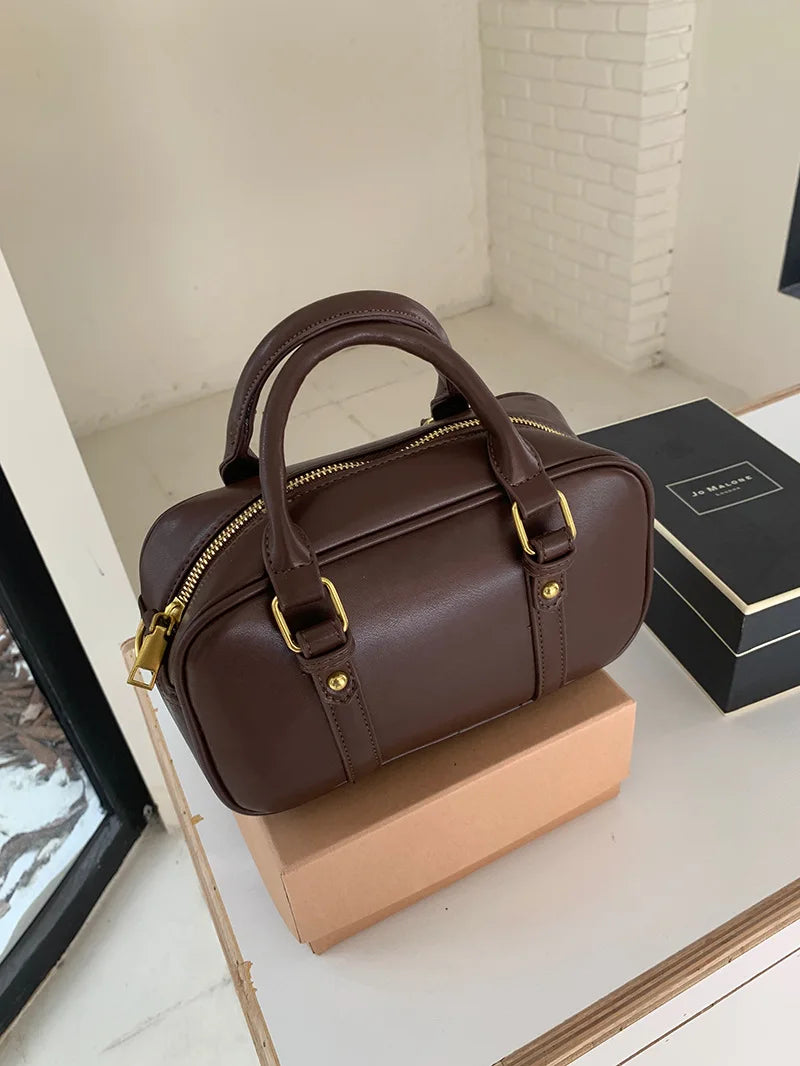 A brown vintage PU leather shoulder bag with gold hardware resting on a light wooden surface.