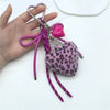 A pink leopard print faux fur charm keychain with a heart and silver beads is held in a hand.