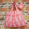 A red and white patterned reusable shopping bag hanging against a brick wall.