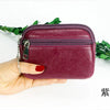 A hand holds a deep purple mini wallet with a zipper and keychain on a white background.