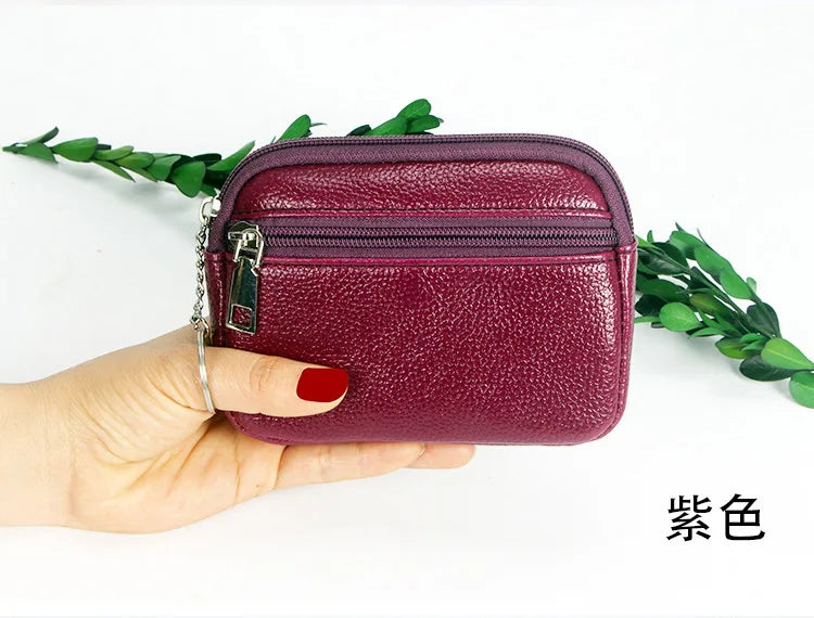 A hand holds a deep purple mini wallet with a zipper and keychain on a white background.