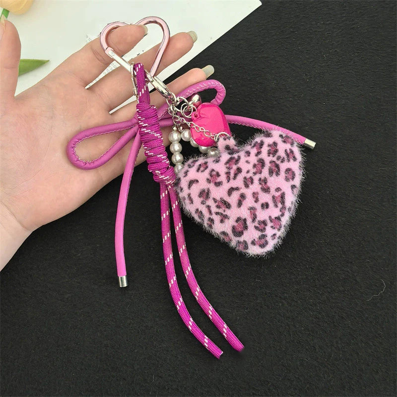 A pink faux fur heart charm keychain with pink and purple string and silver accents