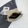 Un bolso de cuero de hombro retro beige claro junto a una chaqueta de traje gris y un libro titulado VIDA.