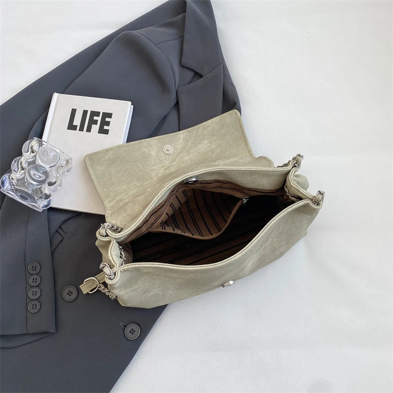 Un bolso de cuero de hombro retro beige claro junto a una chaqueta de traje gris y un libro titulado VIDA.