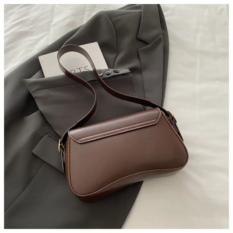 A brown vintage curved flap shoulder bag is shown resting on a gray blazer.