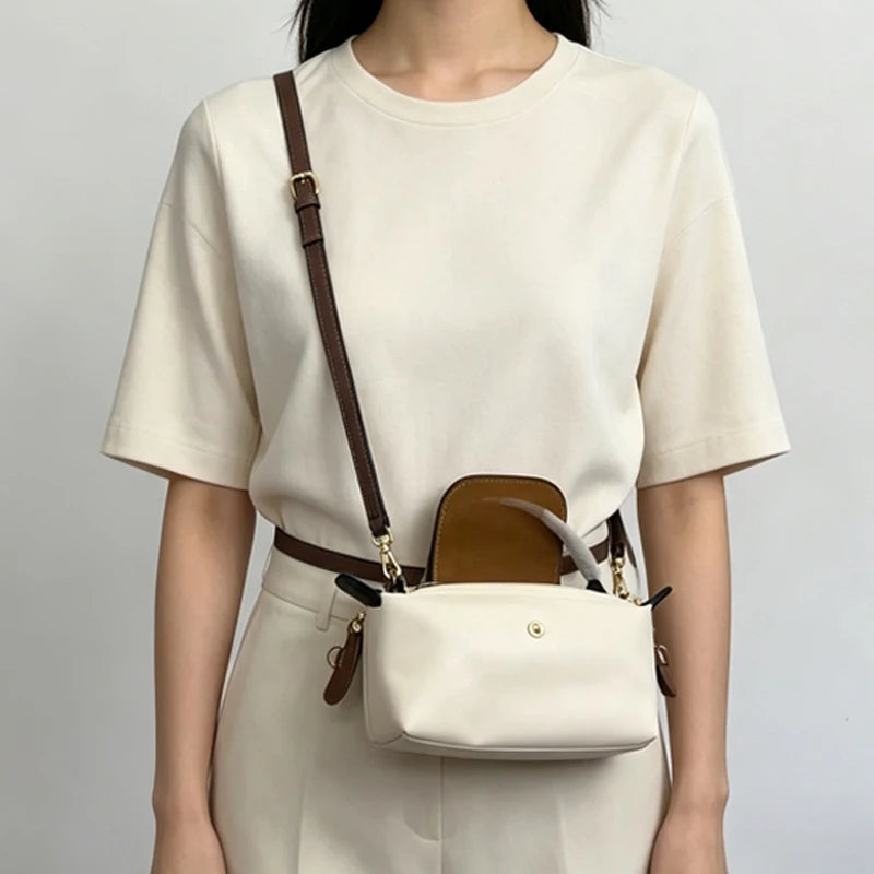 A woman wearing a cream-colored top and trousers, carrying a brown leather crossbody bag with a detachable mini pouch.