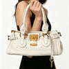 A close-up of a cream vegan leather tote bag with gold hardware being held by a person.