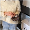 A person wearing a cream faux fur sweater and jeans holds a leopard print PU leather mini tote handbag.