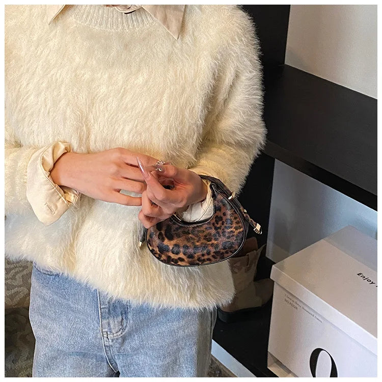 A person wearing a cream faux fur sweater and jeans holds a leopard print PU leather mini tote handbag.