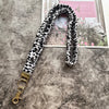Schwarze und weiße gesprenkelte Lanyards mit goldenem Schlüsselclip vor grauem Hintergrund.