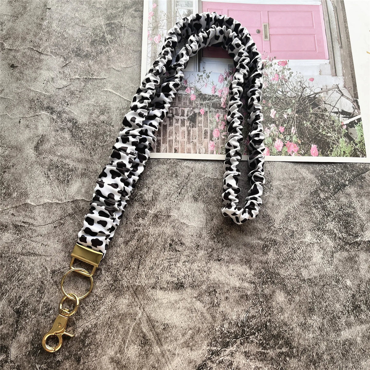 Schwarze und weiße gesprenkelte Lanyards mit goldenem Schlüsselclip vor grauem Hintergrund.