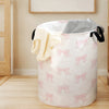A large pink fabric storage basket filled with folded light yellow and gray textiles.