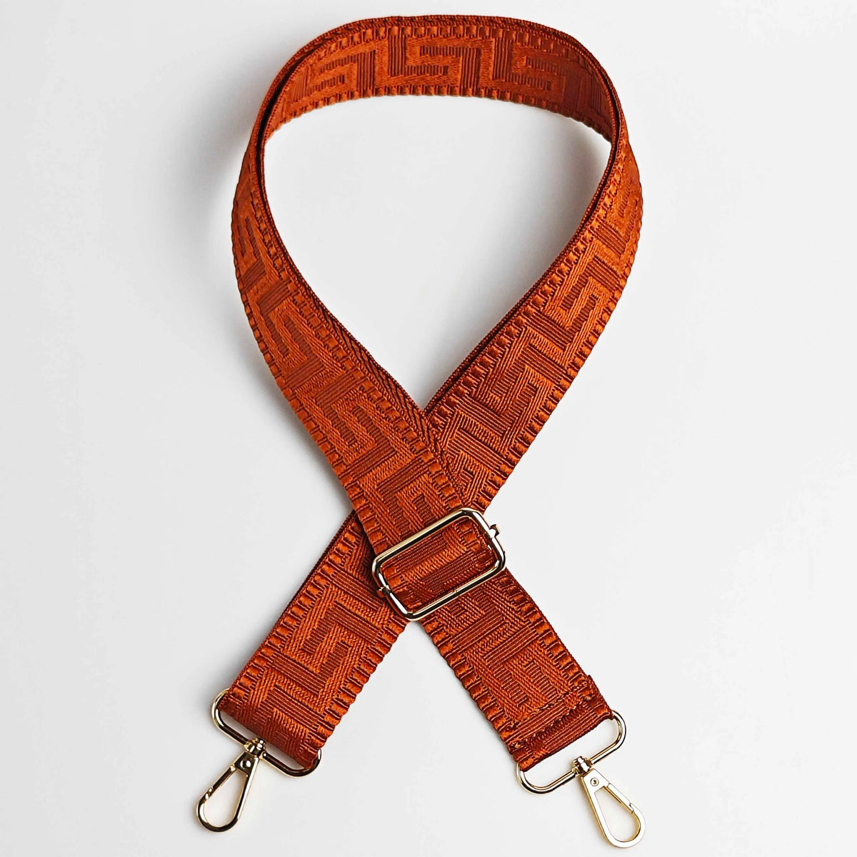 An orange woven strap with a maze pattern is shown crossed and laid flat.