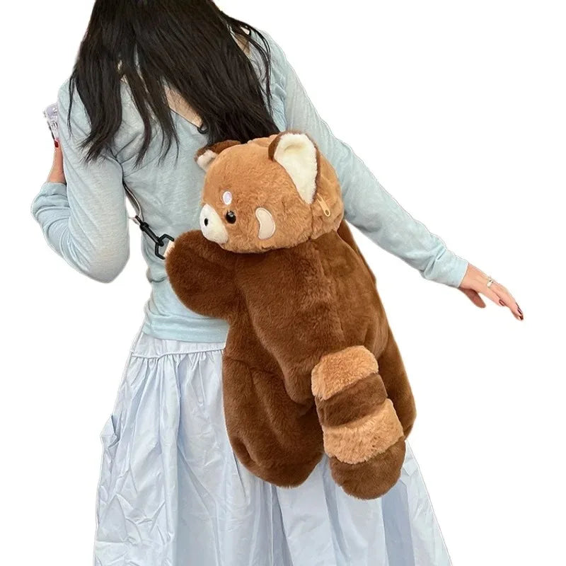 A person is holding a brown red panda plush toy designed as a soft furry crossbody bag.