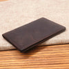A dark brown genuine leather bifold card holder resting on a beige woven fabric surface.
