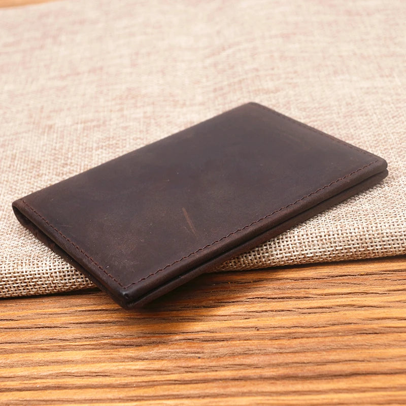 A dark brown genuine leather bifold card holder resting on a beige woven fabric surface.