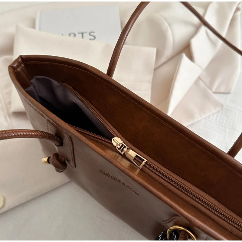 A brown leather tote bag with gold hardware and a zipper is shown open on a white background.