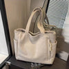 A beige corduroy shoulder bag with a zipper is displayed on a dark surface next to a window.
