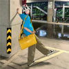 A person wearing a blue shirt and a hat is standing next to a pillar, carrying a yellow faux crocodile tote bag.