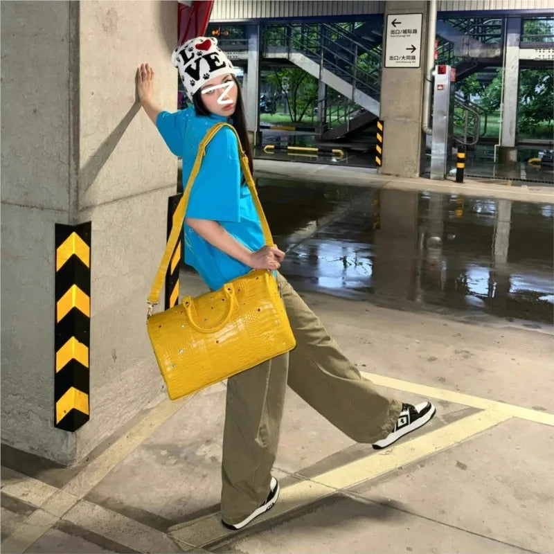 A person wearing a blue shirt and a hat is standing next to a pillar, carrying a yellow faux crocodile tote bag.