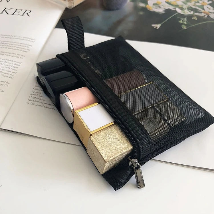 A black mesh cosmetic storage pouch is open, revealing several gold and white makeup products inside.