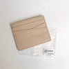 Porte-cartes en cuir véritable beige à design superposé, montré dans une pochette en plastique transparent.