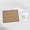 Porte-cartes en cuir véritable couleur camel avec gravure personnalisée, à côté de son emballage plastique transparent.