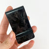 A hand holds a black carbon fiber money clip with an RFID protection feature.