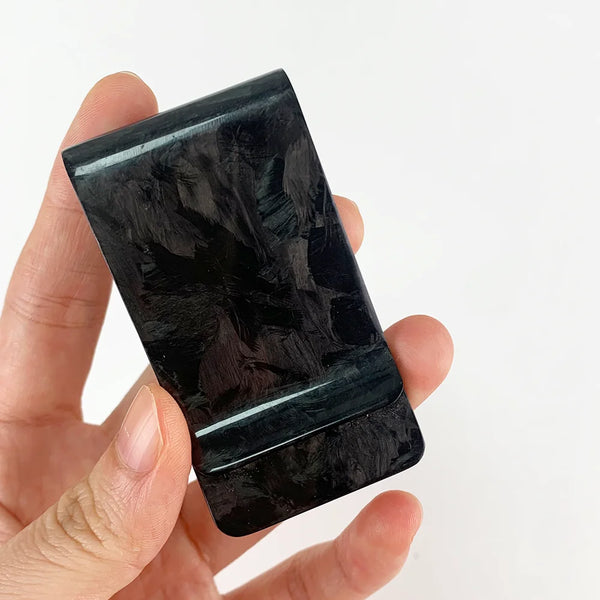 A hand holds a black carbon fiber money clip with an RFID protection feature.